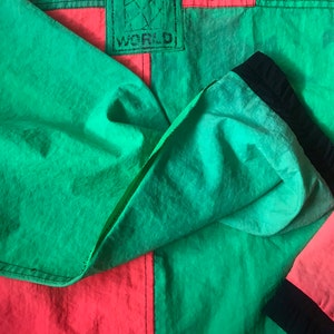 May include: A green and red jacket with a black JAMS WORLD logo patch. The jacket is made of a lightweight, nylon fabric.