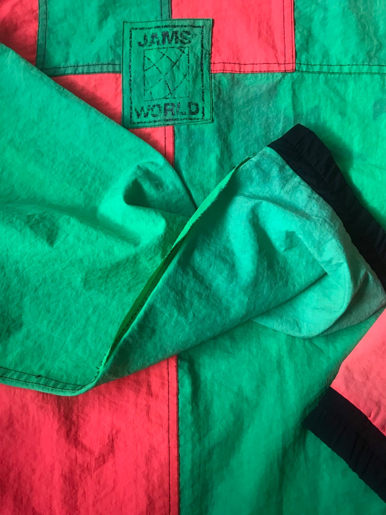May include: A green and red jacket with a black JAMS WORLD logo patch. The jacket is made of a lightweight, nylon fabric.