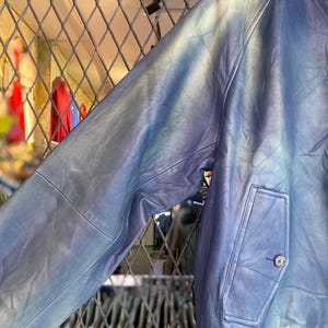 May include: A blue leather jacket with a distinctive tie-dye pattern. The jacket has a buttoned pocket and a ribbed hem. The sleeves display a gradient of blue and white tones. A fashionable outerwear garment.