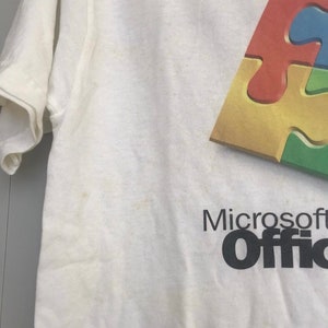 May include: White t-shirt with a colorful puzzle piece design and the text "Microsoft Office" in black.