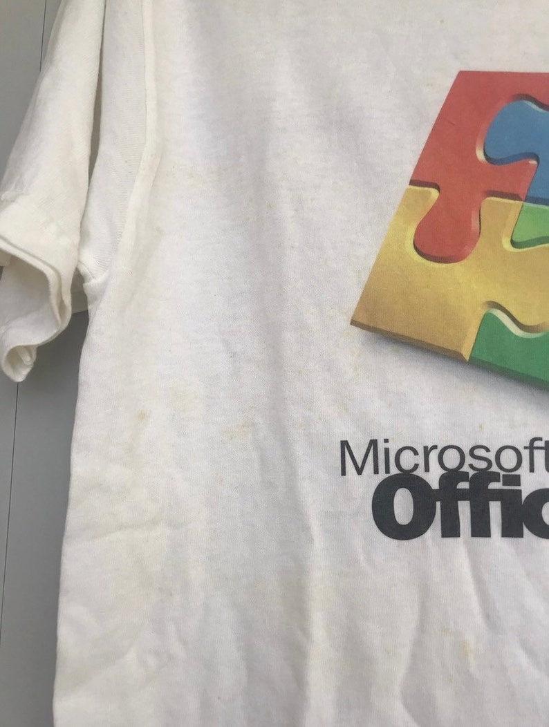 May include: White t-shirt with a colorful puzzle piece design and the text "Microsoft Office" in black.