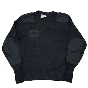 Może przedstawiać: Czarny sweter z dekoltem w serek z wzmocnionymi naszywkami na ramionach, łokciach i kieszeni na piersi. Sweter ma prążkowany dół i mankiety. Etykieta z flagą jest widoczna po wewnętrznej stronie kołnierza.