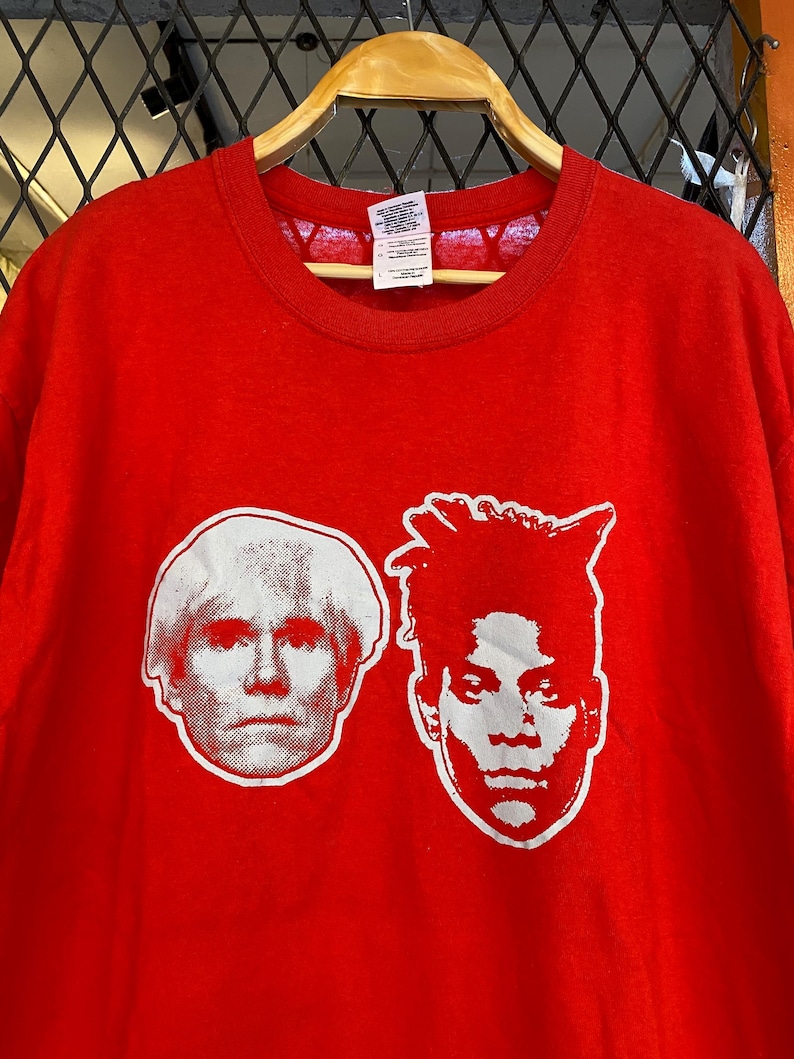 K&ouml;nnte beinhalten: Rotes T-Shirt mit einem wei&szlig;en Grafikdruck der Gesichter von Andy Warhol und Jean-Michel Basquiat.