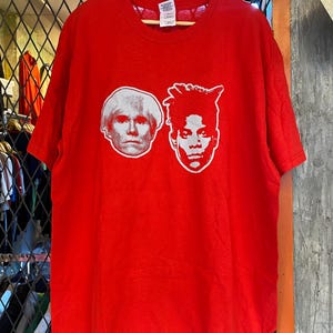 K&ouml;nnte beinhalten: Rotes T-Shirt mit einem wei&szlig;en Aufdruck der Gesichter von Andy Warhol und Jean-Michel Basquiat.