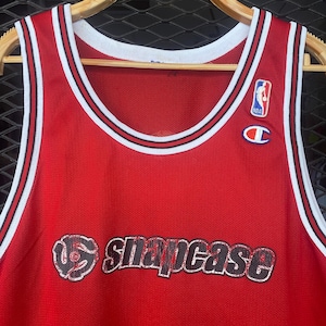 May include: Red basketball jersey with black and white trim. The jersey has a black and white logo with the text "Snapcase" on the front.