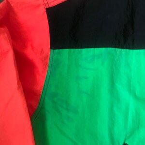 May include: A red, black, and green jacket with a color block design. The jacket is made of a lightweight, water-resistant material.