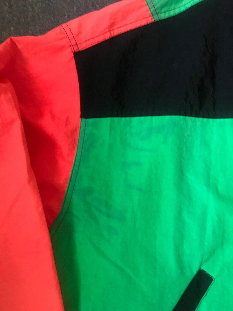 May include: A red, black, and green jacket with a color block design. The jacket is made of a lightweight, water-resistant material.
