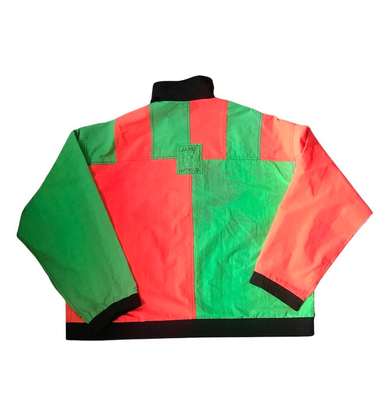 May include: A green and red color block jacket with a black zipper and a black collar. The jacket has a black band around the bottom and the sleeves. The back of the jacket has a small black square patch with the text "JAME WORLD" on it.
