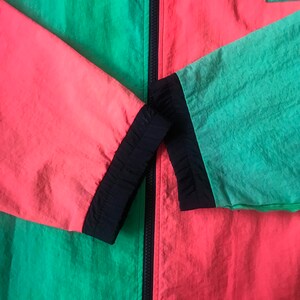 May include: A black, green, and red windbreaker jacket with a zipper closure. The jacket has a black zipper and black trim around the sleeves and collar. The text "J.A.W. WORLD" is printed on the right side of the jacket.