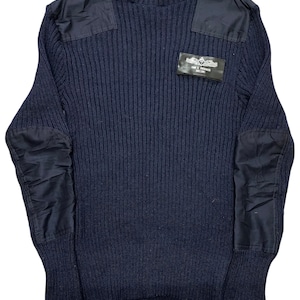 Może przedstawiać: Granatowy sweter z prążkowanej dzianiny z wzmocnionymi naszywkami na ramionach i łokciach. Mała prostokątna naszywka z tekstem i grafiką jest wszyta na piersi. Sweter ma okrągły dekolt i długie rękawy.