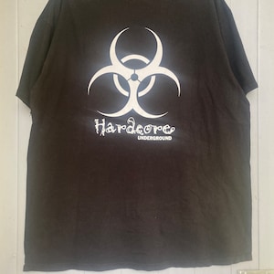 Puede incluir: Camiseta negra con un símbolo de biohazard blanco y el texto "Hardcore Underground" impreso en la espalda.