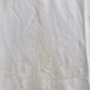 May include: White t-shirt with a faded brown stain. The shirt has the text "Games 2000" printed on the front.