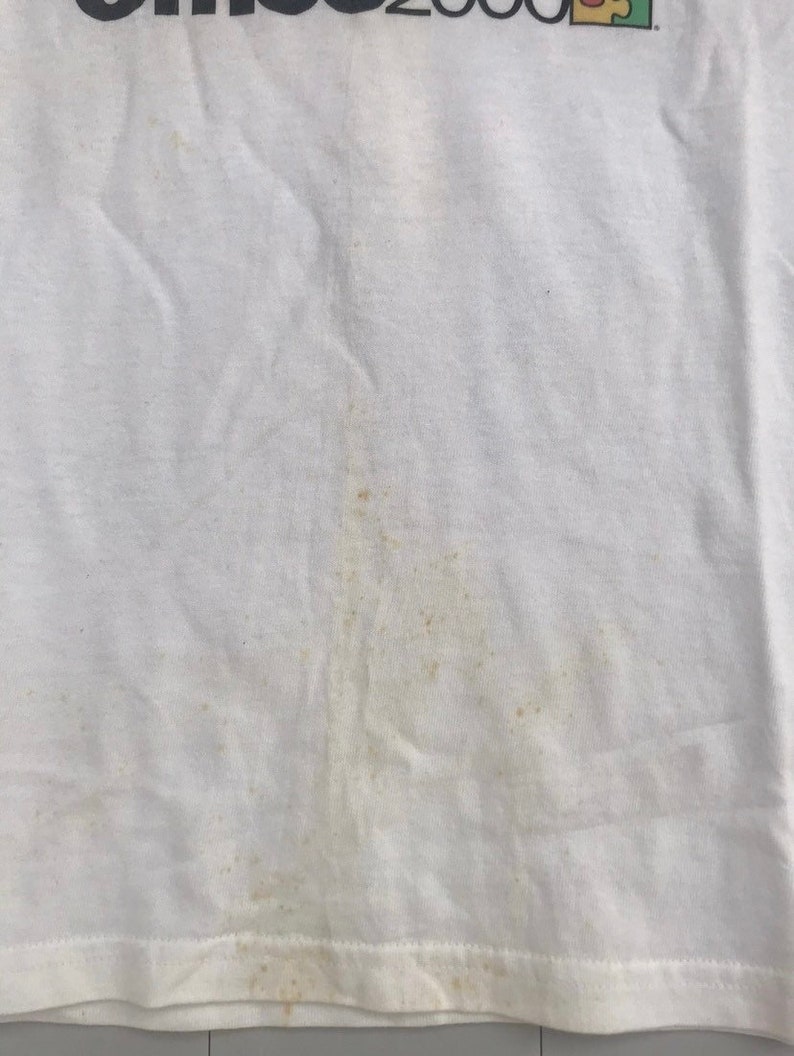May include: White t-shirt with a faded brown stain. The shirt has the text "Games 2000" printed on the front.