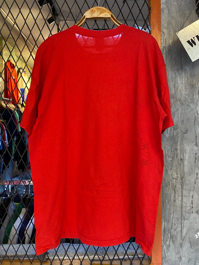 K&ouml;nnte beinhalten: Ein einfarbiges rotes T-Shirt mit Rundhalsausschnitt. Das Shirt h&auml;ngt an einem Holzb&uuml;gel.