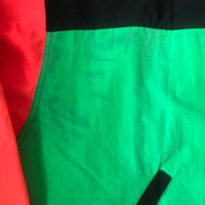 May include: A close-up of a jacket with red, black, and green panels. The fabric is a shiny nylon.