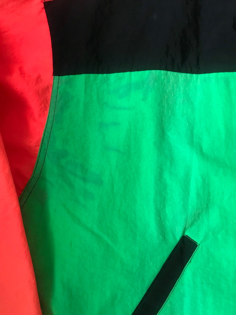 May include: A close-up of a jacket with red, black, and green panels. The fabric is a shiny nylon.