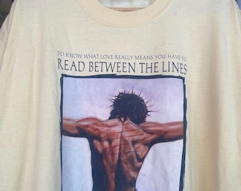 May include: A yellow t-shirt featuring a graphic of a man with a crown of thorns and the text "To know what love really means you have to read between the lines."