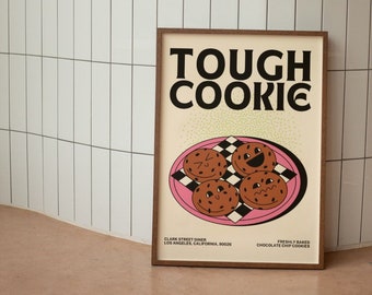May include: A brown framed poster with the text "TOUGH COOKIE" in white letters. The poster has a pink background with a white checkered pattern and four chocolate chip cookies with smiley faces on them. The poster also includes the text "CLARK STREET DINER LOS ANGELES, CALIFORNIA, 90026" and "FRESHLY BAKED CHOCOLATE CHIP COOKIES".