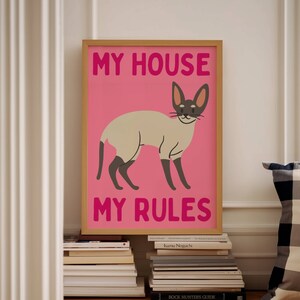 K&ouml;nnte beinhalten: Ein rosa Poster mit einer wei&szlig;en Katze und dem Text "MY HOUSE MY RULES" in fetten rosa Buchstaben.