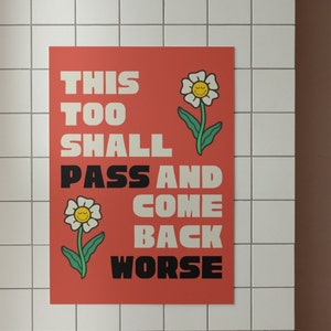 Pu&ograve; includere: Un poster rosso con testo bianco che recita "This Too Shall Pass And Come Back Worse". Il poster presenta due fiori bianchi con facce sorridenti gialle.