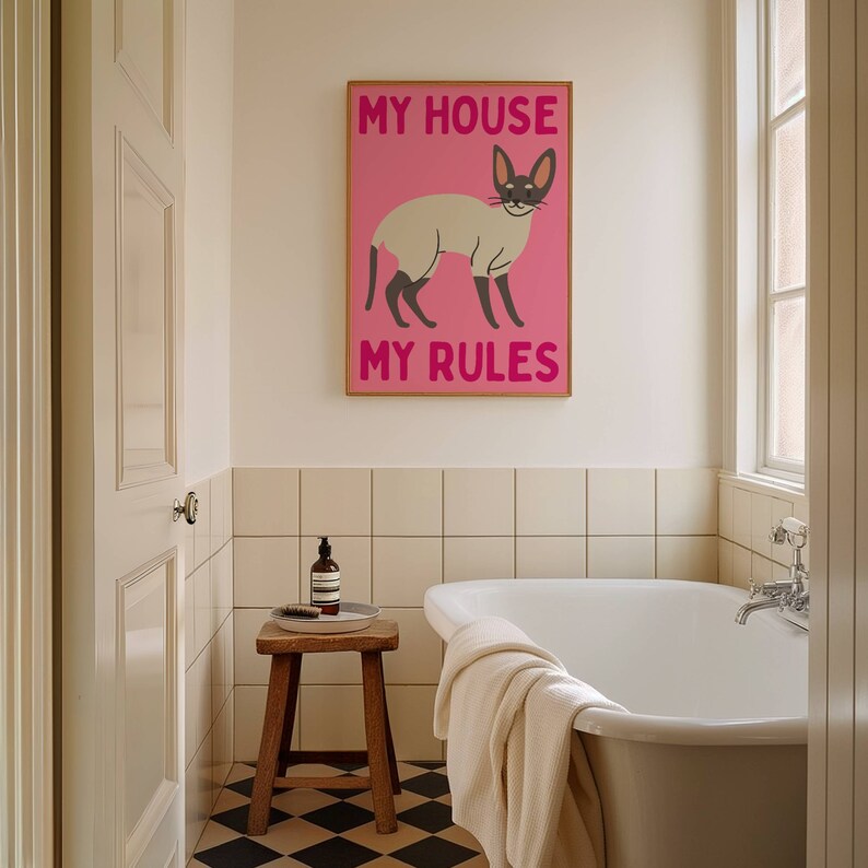 K&ouml;nnte beinhalten: Ein rosa-wei&szlig;es Poster mit einer Katzenillustration und dem Text "My House My Rules". Das Poster h&auml;ngt an einer wei&szlig;en gekachelten Wand in einem Badezimmer mit einer wei&szlig;en Badewanne und einem Holzhocker.