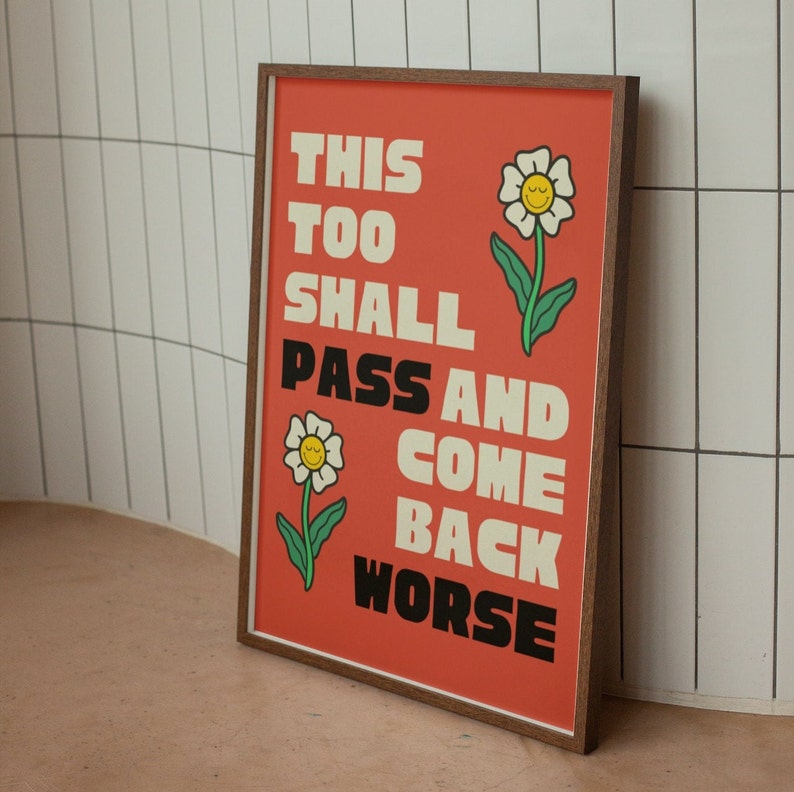 Pu&ograve; includere: Una stampa incorniciata con sfondo rosso e testo bianco che recita "This Too Shall Pass And Come Back Worse". La stampa presenta due fiori di cartone animato con facce sorridenti.