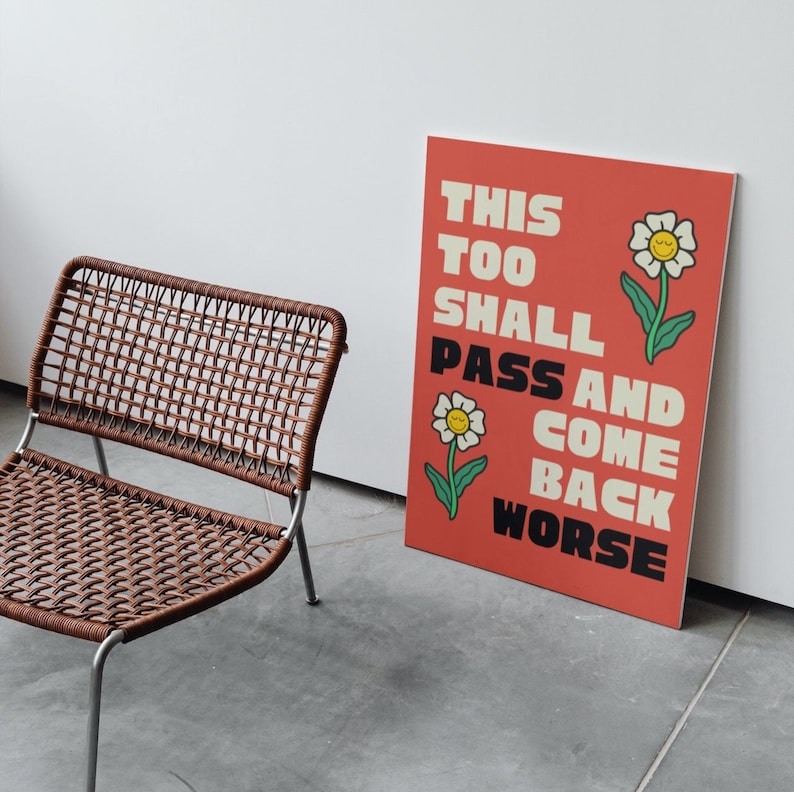 Pu&ograve; includere: Un poster rosso con il testo "This Too Shall Pass And Come Back Worse" in lettere bianche e nere. Il poster presenta due fiori bianchi con centri gialli e facce sorridenti.