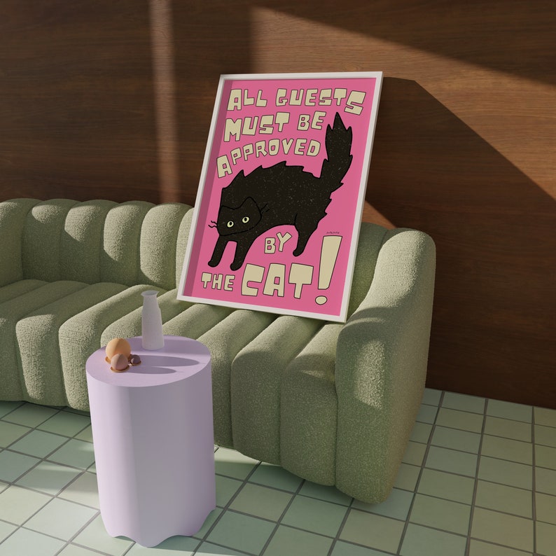 May include: A pink and white framed print with a black cat and the text "All guests must be approved by the cat!"