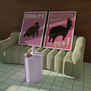 May include: Two pink posters with black cat illustrations and text. The poster on the left says "Guilty" and the poster on the right says "All guests must be approved by the cat!" The posters are hanging on a wall above a green sofa.