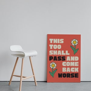 Pu&ograve; includere: Un poster rosso con il testo "This Too Shall Pass And Come Back Worse" in bianco e nero. Il poster ha due fiori bianchi con centri gialli e facce sorridenti.