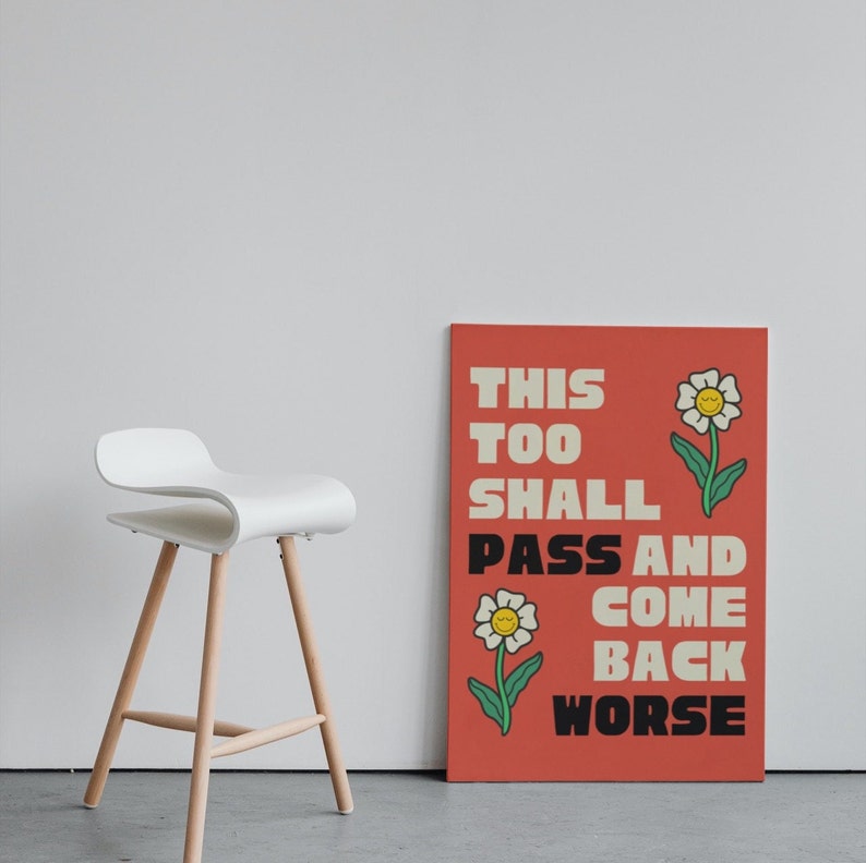 Pu&ograve; includere: Un poster rosso con il testo "This Too Shall Pass And Come Back Worse" in bianco e nero. Il poster ha due fiori bianchi con centri gialli e facce sorridenti.