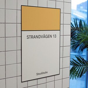 May include: A white sign with black text and a yellow stripe at the top. The sign reads "STRANDV&Auml;GEN 13 Stockholm".