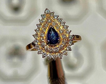 May include: A gold ring with a teardrop-shaped blue sapphire surrounded by a halo of small diamonds.