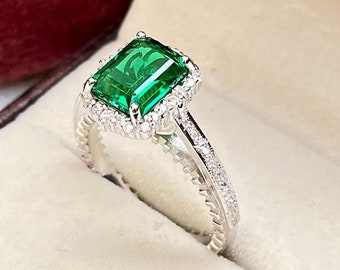 May include: A silver ring with a large emerald green gemstone surrounded by smaller diamonds. The ring is in a velvet ring box.