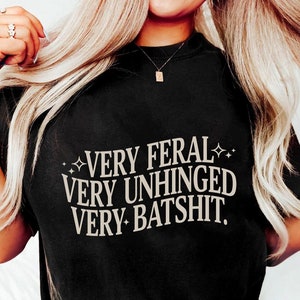 May include: Black t-shirt with the text "VERY FERAL VERY UNHINGED VERY BATSHIT." in beige lettering.