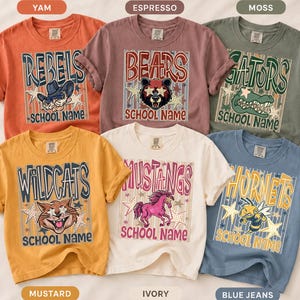 May include: Six short-sleeve t-shirts in yam, espresso, moss, mustard, ivory, and blue jeans colors. Each shirt features a graphic with a mascot, stars, vertical stripes, and the text SCHOOL NAME. Mascots include a cowboy, bear, alligator, cat, horse, and hornet.