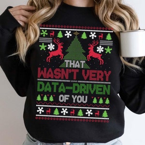 May include: Black sweatshirt with a festive Christmas design. The design includes red reindeer, green Christmas trees, and snowflakes. The text "THAT WASN'T VERY DATA-DRIVEN OF YOU" is prominently displayed in red and green.