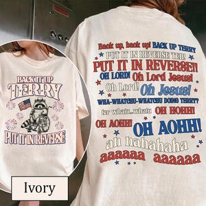 May include: Ivory-colored t-shirt with the text "BACK IT UP TERRY" and "PUT IT IN REVERSE". The front graphic features a raccoon in a wheelchair holding an American flag. The back has more text.
