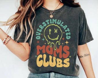 Può includere: T-shirt grigio scuro con le parole "OVERSTIMULATED MOMS CLUBS" in un font retrò colorato. La maglietta presenta una grafica con una faccina sorridente che si scioglie. La maglietta è uno stile casual e confortevole.