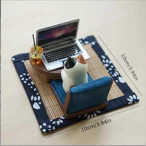 Peut inclure: Figurine miniature d'un chat assis devant un ordinateur portable. Le chat est assis sur une chaise bleue, avec une boisson et une petite table. L'ensemble est posé sur un tapis en bambou de 10 cm de côté, avec une bordure bleue à motifs.