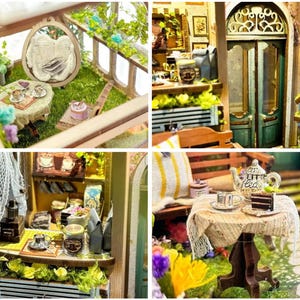 May include: A miniature dollhouse scene with a tea party set up in a garden. There is a small table with a teapot, cups, and a plate of pastries. The garden is filled with green plants and flowers. The dollhouse is made of wood and has a white picket fence.