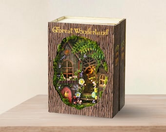 May include: A miniature wooden house with a light inside, surrounded by greenery and flowers, is displayed in a book-shaped box with the words "Forest Wonderland" on the cover.