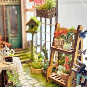 May include: A miniature dollhouse scene with a wooden porch, a small table with a teapot and teacups, and a wooden plant stand with potted plants and a butterfly.