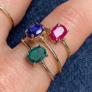K&ouml;nnte beinhalten: Drei goldene Ringe mit ovalen Edelsteinen. Der obere Ring hat einen blauen Saphir, der mittlere Ring einen roten Rubin und der untere Ring einen gr&uuml;nen Smaragd.