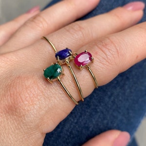 K&ouml;nnte beinhalten: Drei goldene Ringe mit ovalen Edelsteinen. Die Ringe sind auf einem Finger &uuml;bereinander gelegt. Der obere Ring hat einen blauen Edelstein, der mittlere Ring einen gr&uuml;nen Edelstein und der untere Ring einen roten Edelstein.