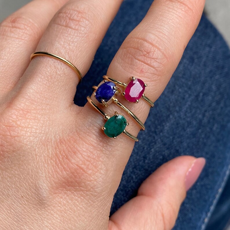 K&ouml;nnte beinhalten: Drei goldene Ringe mit ovalen Edelsteinen. Der obere Ring hat einen rosafarbenen Edelstein, der mittlere Ring einen blauen Edelstein und der untere Ring einen gr&uuml;nen Edelstein.