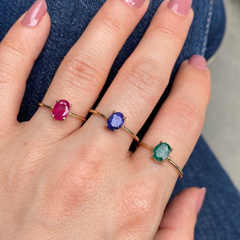 K&ouml;nnte beinhalten: Drei goldene Ringe mit ovalen Edelsteinen. Die Ringe zeigen einen roten Rubin, einen blauen Saphir und einen gr&uuml;nen Smaragd.