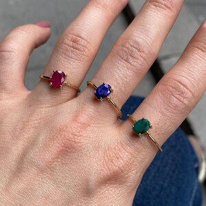 K&ouml;nnte beinhalten: Drei goldene Ringe mit ovalen Edelsteinen. Die Ringe befinden sich an einem Finger. Die Edelsteine sind rot, blau und gr&uuml;n.