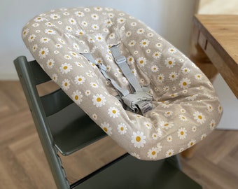 May include: A beige high chair with a daisy print cushion and a gray five-point harness.