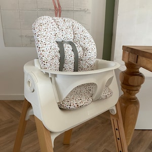 Op de afbeelding: Witte hoge stoel met houten poten en een zitkussen met bloemenprint.